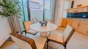 A dining area with a round table and four chairs, a potted plant, and a view of a building through a glass door. - Casa Loba Luxe Unit 3 w/private pool and garden (Rincon)