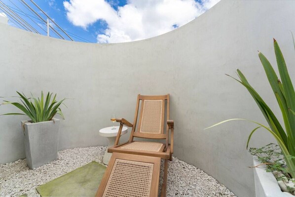 Un pequeño espacio al aire libre con una silla de madera y una mesa pequeña, rodeado de guijarros y plantas en macetas.