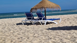 Una spiaggia con due lettini bianchi e un ombrellone di paglia.