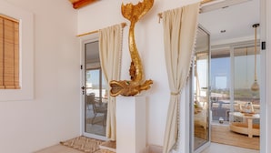 Un interno moderno con una porta vetrata che si apre su un balcone, un elemento decorativo dorato al muro e un tappeto a motivi sul pavimento.