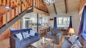 A cozy living area with a wooden staircase, a kitchen in the background, and a dining area with a table and chairs. - Cabin w/ Deck, Fire Pit & Big Bear Lake Access! (Big Bear)