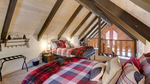 A cozy attic bedroom with a sloped ceiling, wooden beams, a bed with a plaid blanket, a nightstand, and a small desk. - Cabin w/ Deck, Fire Pit & Big Bear Lake Access! (Big Bear)
