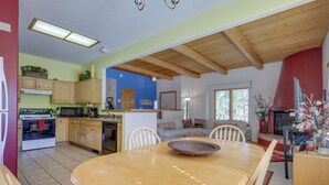 A spacious kitchen with wooden cabinets, a dining table with chairs, and a large window providing natural light. - Serene Amalia Cabin w/ Deck & Mountain Views (Amalia)