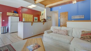 A living room with a sofa, a coffee table, and a kitchen area with a refrigerator and cabinets. - Serene Amalia Cabin w/ Deck & Mountain Views (Amalia)