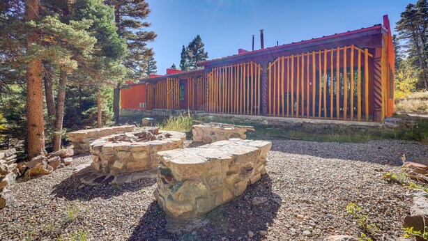 A rustic cabin with a red roof and wooden vertical supports, surrounded by a gravel area and large rocks. - Amalia Mountain Getaway w/ Deck, Fireplace! (Amalia)