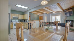 A spacious kitchen with wooden cabinets, a dining table with chairs, and a large window providing natural light. - Amalia Mountain Getaway w/ Deck, Fireplace! (Amalia)