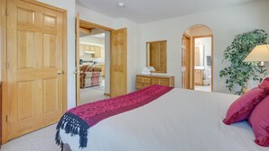 A bedroom with a large bed, wooden doors, a dresser, a mirror, and a potted plant. - Charming Amalia Retreat w/ Fireplace & Grill! (Amalia)