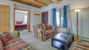A cozy living room with a sofa, a small table, and a lamp. There is a door leading to another room with a bed. - Charming Amalia Retreat w/ Fireplace & Grill! (Amalia)