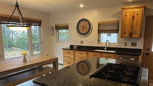 A kitchen with wooden cabinets, a granite countertop, a stove, and a window with a view of trees. - 4 Seasons Superior Beach House (Marquette)