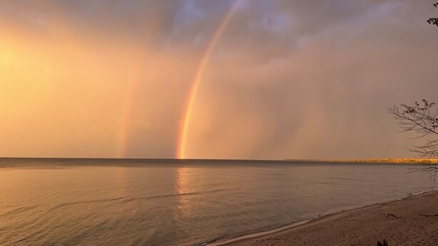A beach with a rainbow over the water. - 4 Seasons Superior Beach House (Marquette)