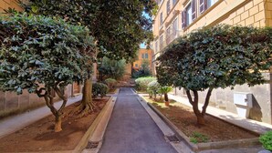 A narrow alleyway flanked by trees and buildings, leading to a distant structure. - Elegant and spacious suite in upscale setting within walking distance of Villa Borghese. (Roma)