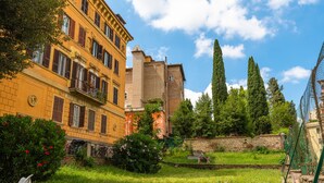 A courtyard with a grassy area, a white chair, and a building with multiple windows and balconies. - Elegant and spacious suite in upscale setting within walking distance of Villa Borghese. (Roma)