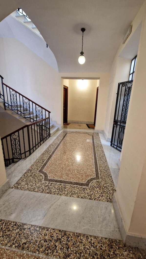 A spacious hallway with a marble floor, a staircase with black railings, and a ceiling light. - Elegant and spacious suite in upscale setting within walking distance of Villa Borghese. (Roma)
