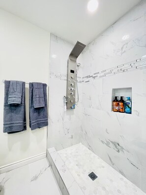 Shower area features a wall-mounted showerhead and control panel, along with a shelf for toiletries.