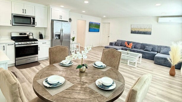 Una cocina moderna con armarios blancos, electrodomésticos de acero inoxidable y un comedor con una mesa redonda y sillas acolchadas.
