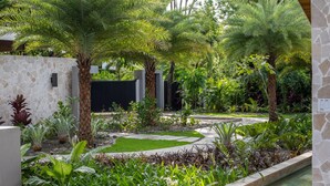 Un jardín ajardinado con palmeras, un muro de piedra y un sendero.