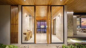 Una entrada de hotel moderna con techo de madera, puertas de vidrio y vista al interior.