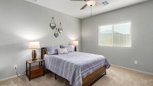 Une chambre à coucher comprenant un lit, deux tables de chevet avec des lampes, un ventilateur de plafond et une fenêtre avec des stores.