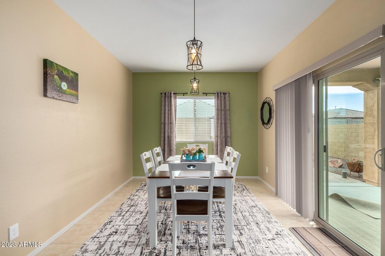 A dining area with a table set for four, a chandelier, and a view through a glass door.