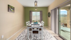 Un coin repas avec une table dressée pour quatre personnes, un lustre et une vue sur l’extérieur, visible à travers une porte vitrée.
