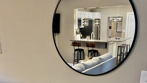 Een ronde spiegel die een moderne keuken toont met een bar, een bank en een potplant op een bijzettafeltje.