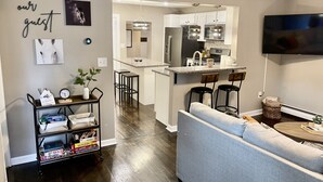 Een moderne woonkamer met een grijze bank, een salontafel en een aan de muur bevestigde televisie.