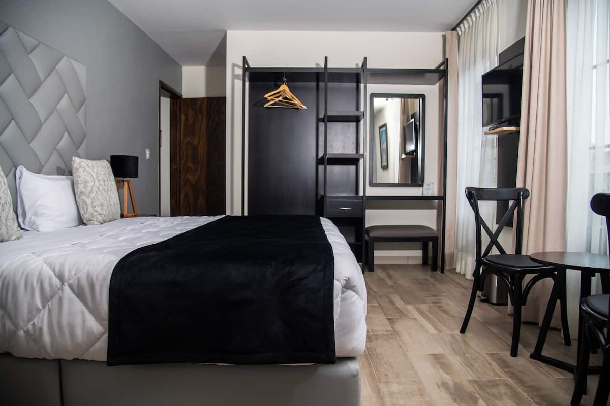 A modern hotel room with a large bed, a desk, a chair, and a hanging coat rack.