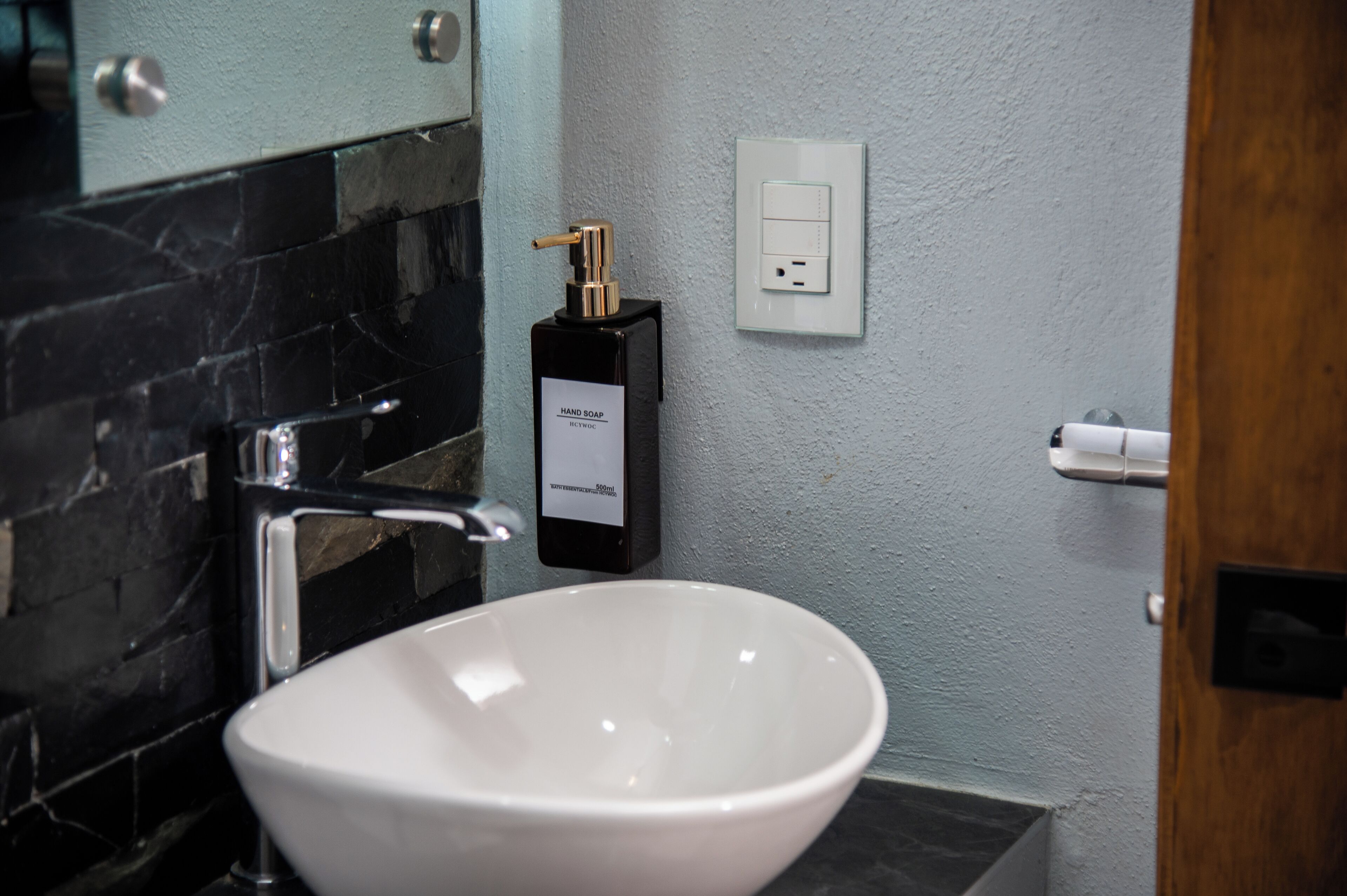 A bathroom with a white sink, a black soap dispenser, and a mirror.