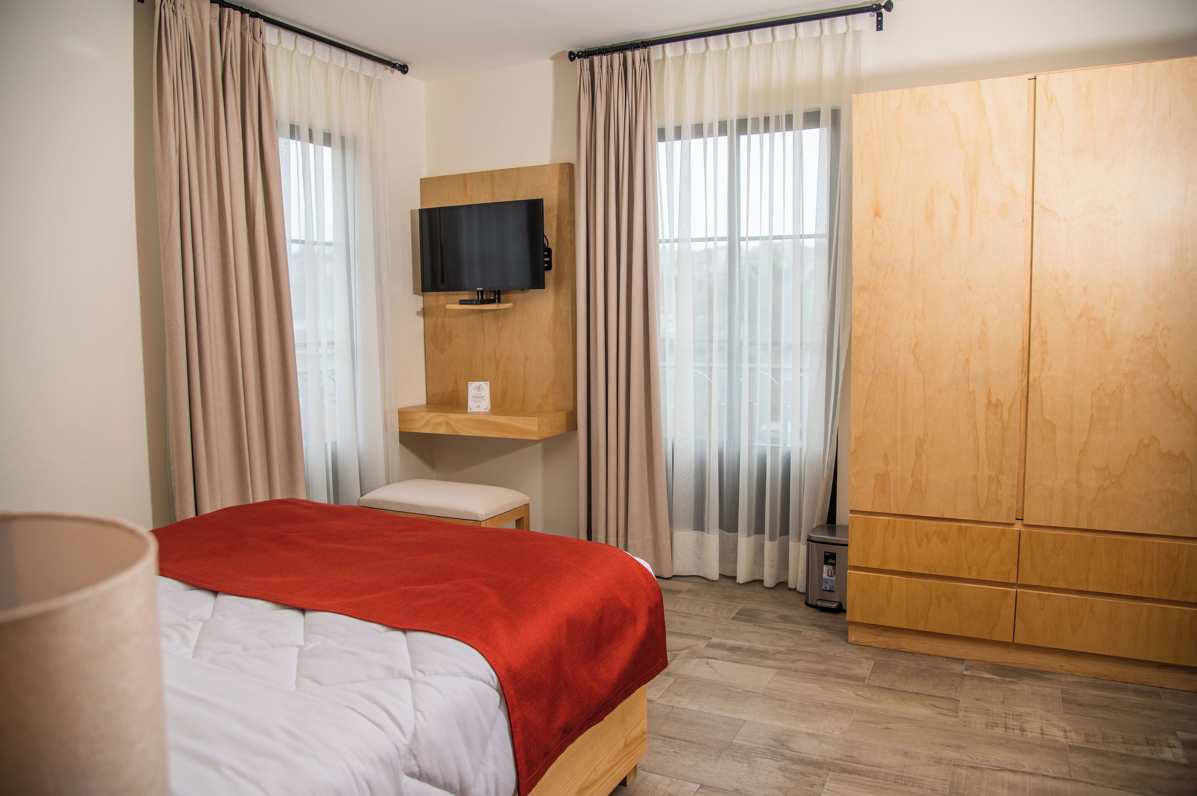 Une chambre d’hôtel avec un lit, un téléviseur fixé sur un panneau en bois, une armoire et une petite table.