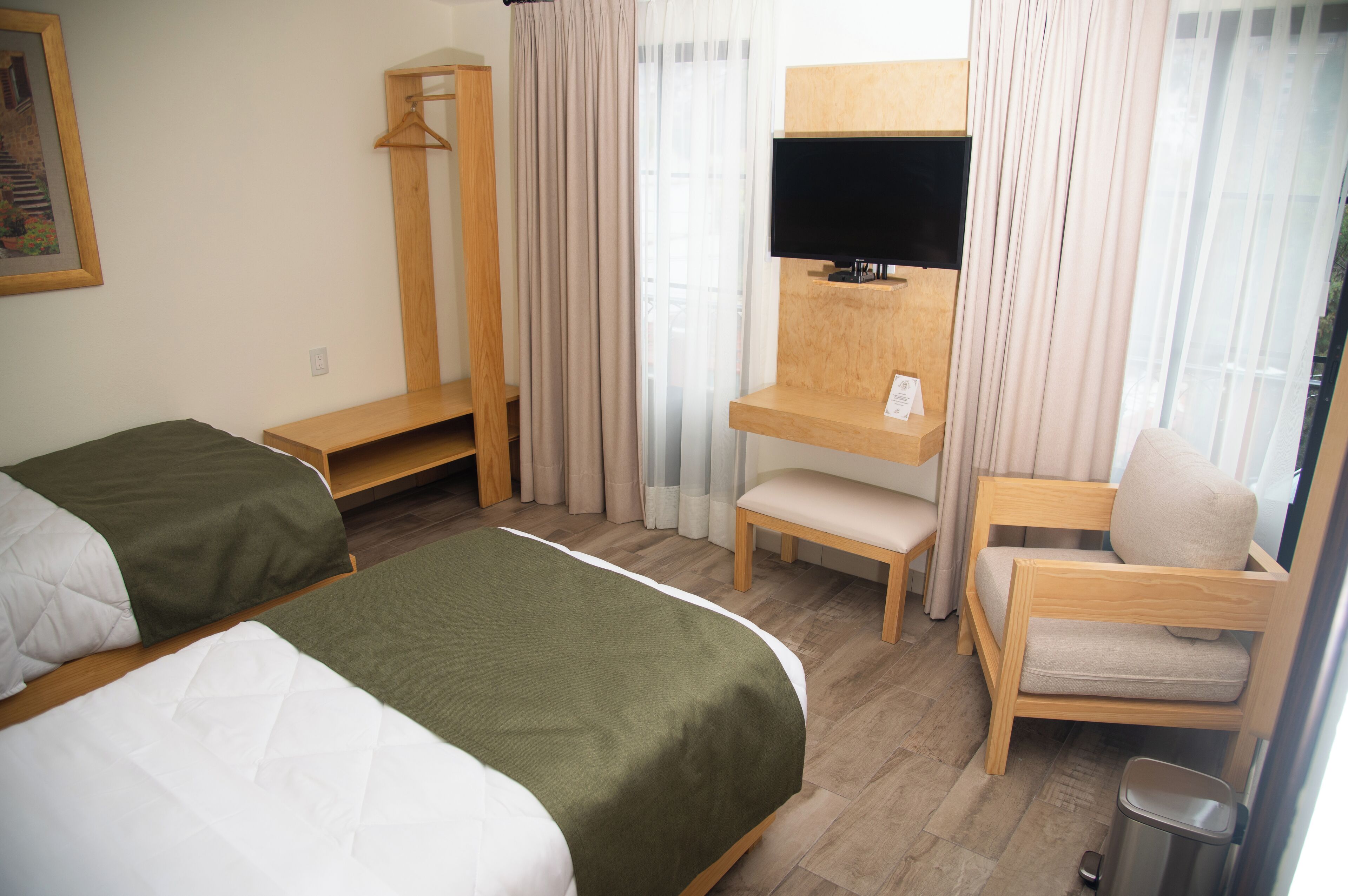 Une chambre d’hôtel avec deux lits, un bureau avec une télévision, une chaise et une fenêtre avec des rideaux.