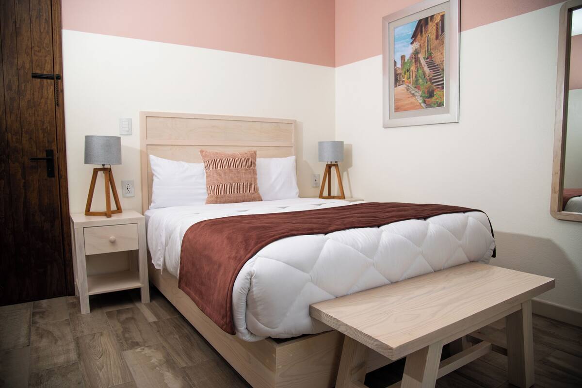 A neatly arranged bedroom with a bed, bedside tables, a bench, and a painting on the wall.