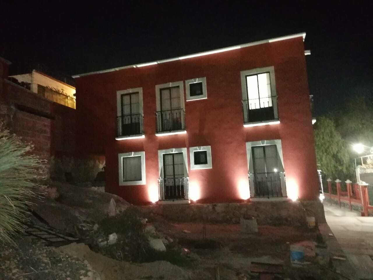 A red building with multiple windows and balconies, illuminated by exterior lighting.