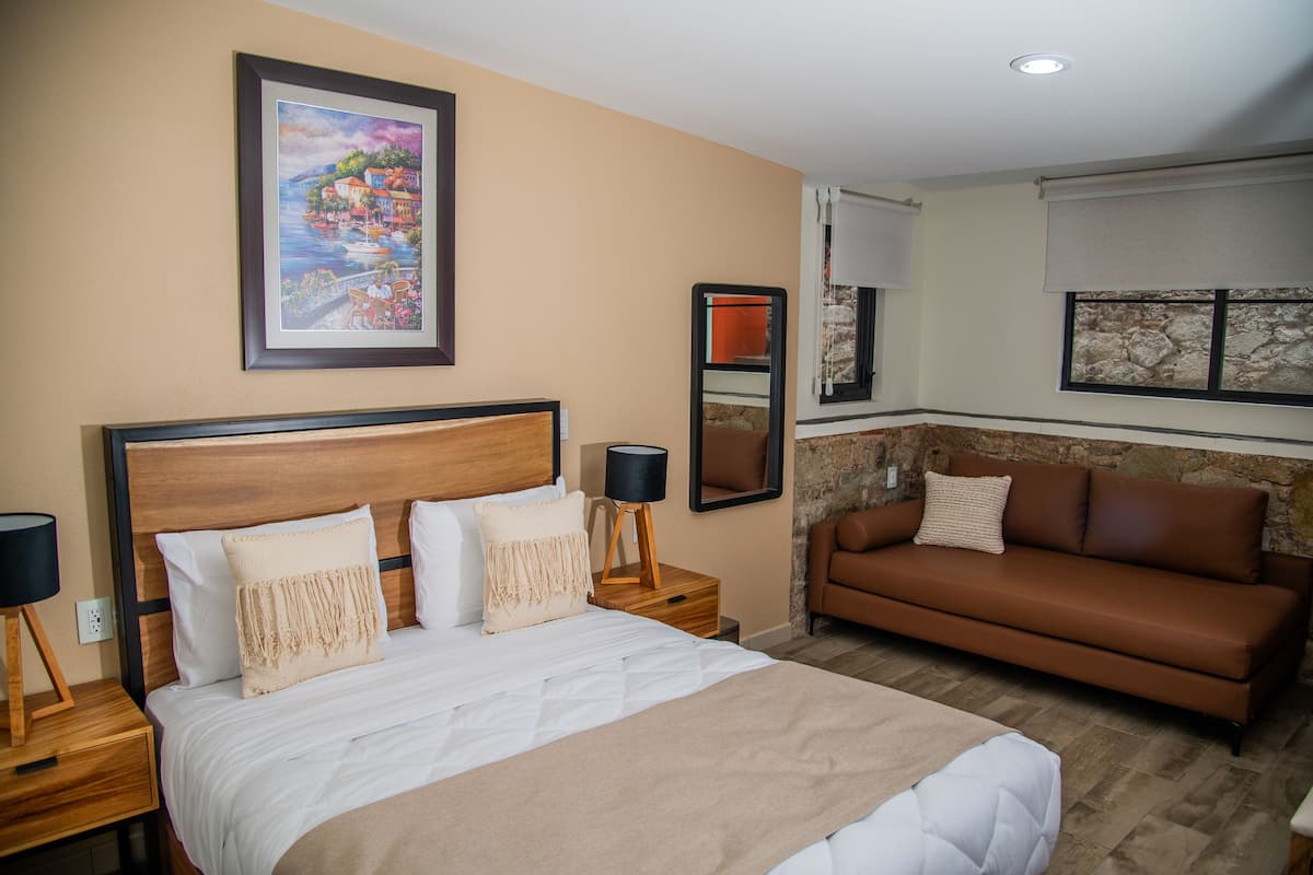 A hotel room with a large bed, a brown sofa, a painting on the wall, and a stone accent wall.