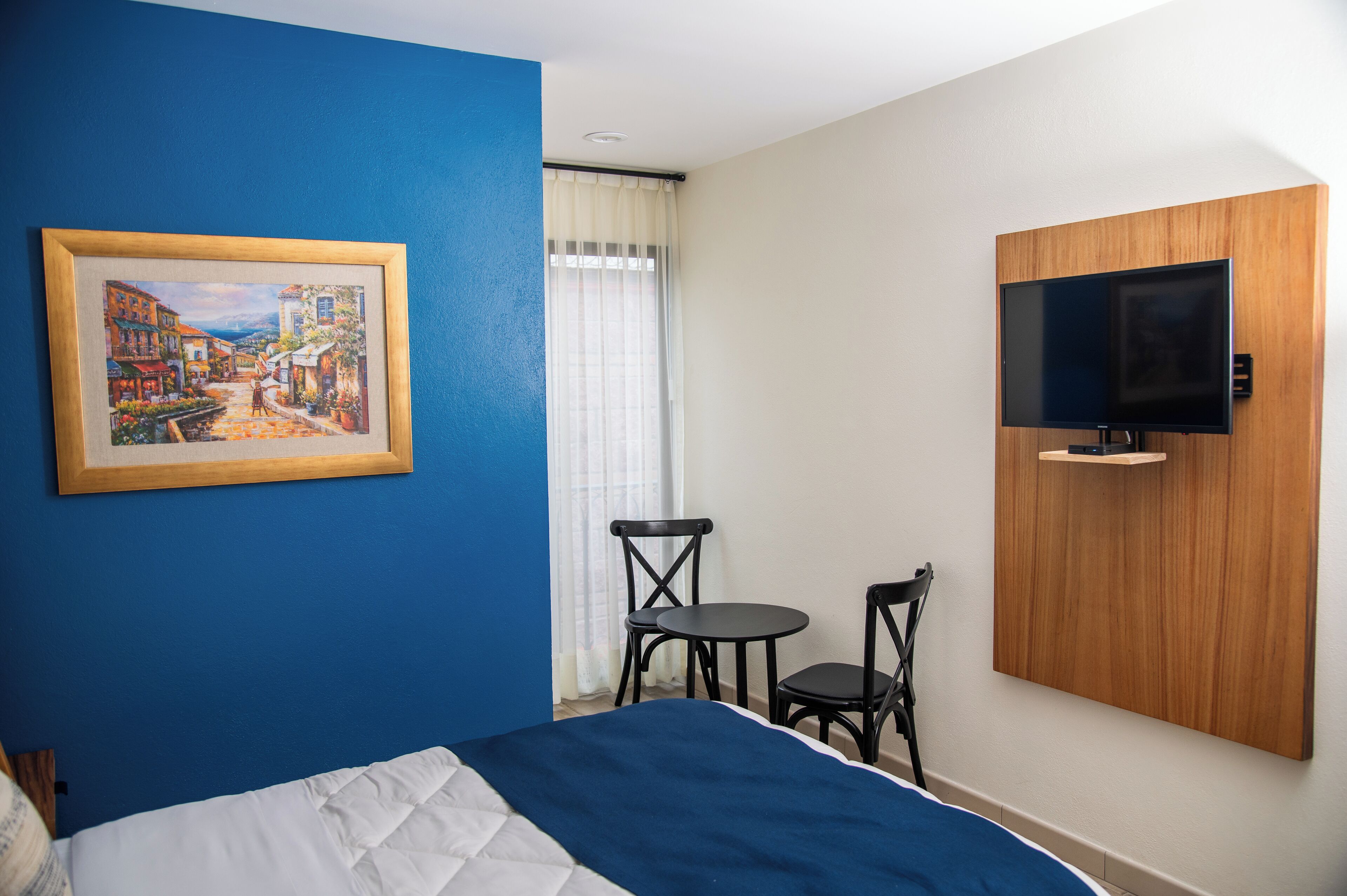 Une chambre d’hôtel avec un lit, un tableau, une télévision et deux chaises.