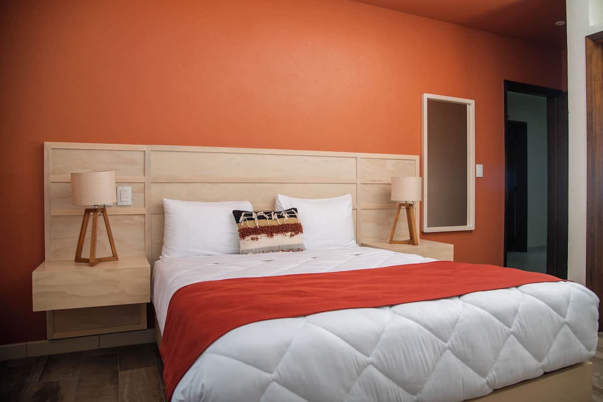 A hotel room with a large bed, wooden headboard, two bedside tables with lamps, and a red throw blanket.