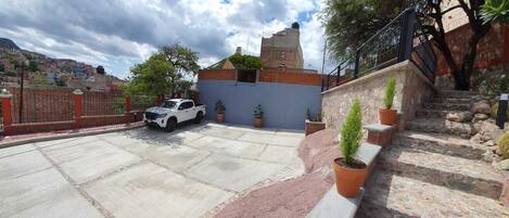 Un aparcamiento con una camioneta pickup blanca, una escalera que conduce a un edificio y plantas en macetas a lo largo de los escalones.