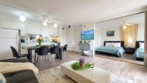A modern apartment with a dining area, kitchen, and a bedroom with a bed and a TV.