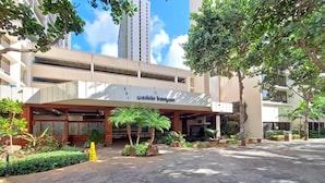 A building with a sign reading "Wai Kikibanyan" and a covered entrance area with palm trees and potted plants.