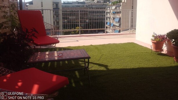 Ein Balkon mit einem roten Stuhl, einem kleinen Tisch und Topfpflanzen.