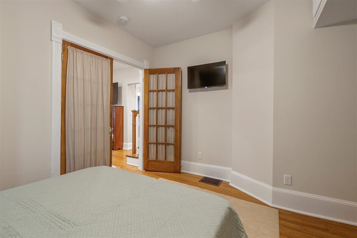 A bedroom with a bed, a television mounted on the wall, and a door leading to another room.
