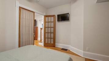 A bedroom with a bed, a television mounted on the wall, and a door leading to another room.