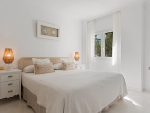 Um quarto espaçoso com uma cama grande, duas mesas de cabeceira e uma janela com vista para o verde lá fora.