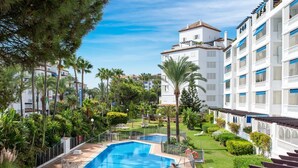 A resort with a swimming pool surrounded by lush greenery and palm trees. - Apartment in Las Gaviotas for 6 people | 2-108 (Puerto Banús - Marbella)