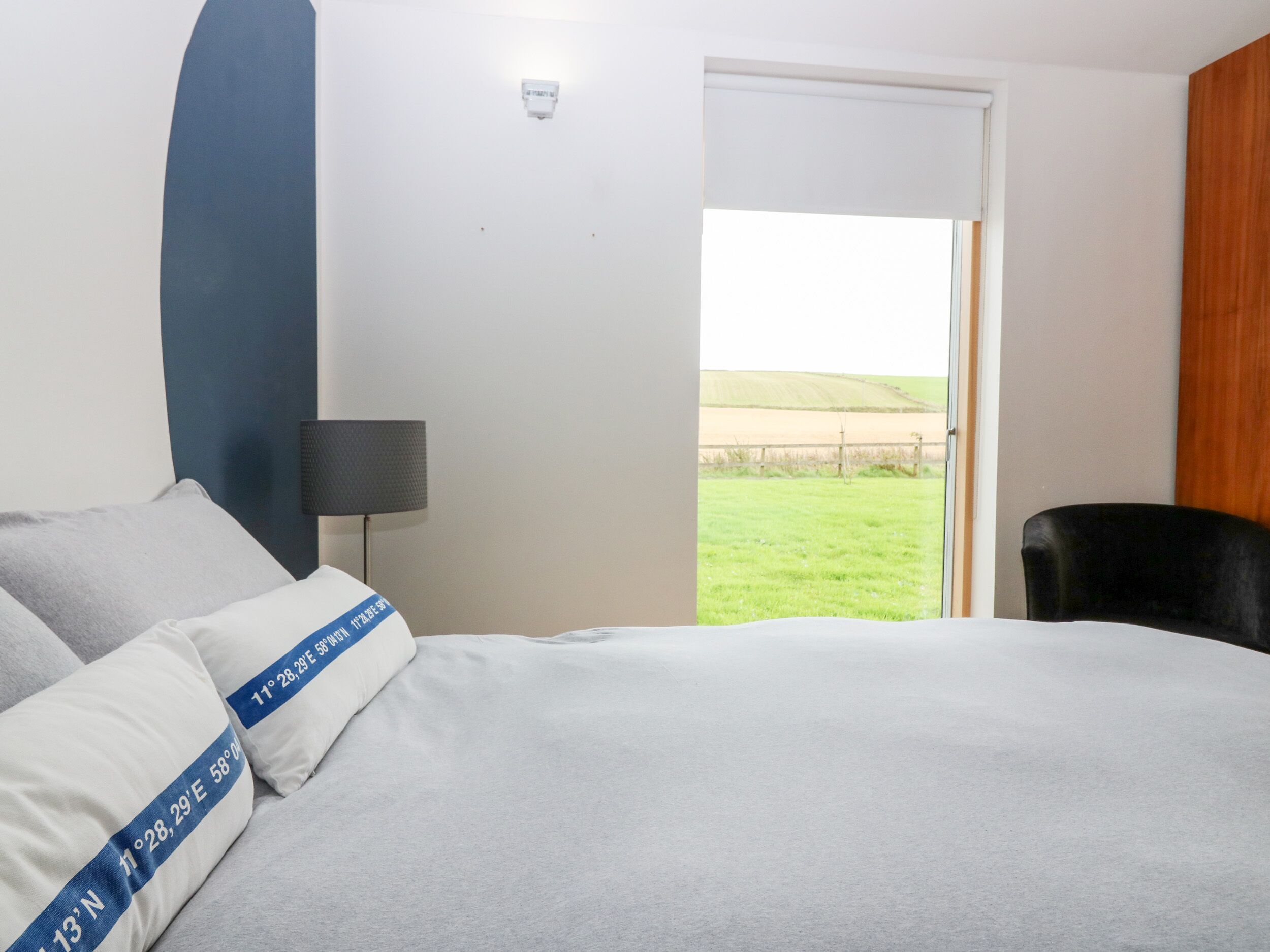 A hotel room with a bed, a chair, a lamp, and a view of a grassy field through a door.