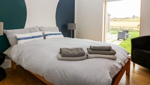 Ein Schlafzimmer mit einem Bett, Kissen, einer Lampe und Blick auf einen Garten durch eine Schiebetür.