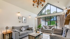 A spacious living room with a high ceiling, large windows, and a modern chandelier.