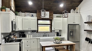 A modern kitchen with white cabinets, a central island with stools, a stainless steel refrigerator, and a window with a view of the outdoors. - Cabin overlooking lake with great fishing!!!  (Pelahatchie)