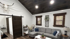A living room with a sectional sofa, a coffee table, a chandelier, and a large wooden door. - Cabin overlooking lake with great fishing!!!  (Pelahatchie)