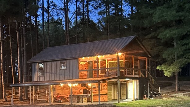 A two-story log cabin with a covered porch and a reflection in the water. - Cabin overlooking lake with great fishing!!!  (Pelahatchie)