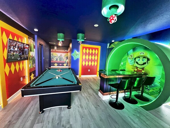 A pool table in a room with colorful walls and a Mario-themed bar area.